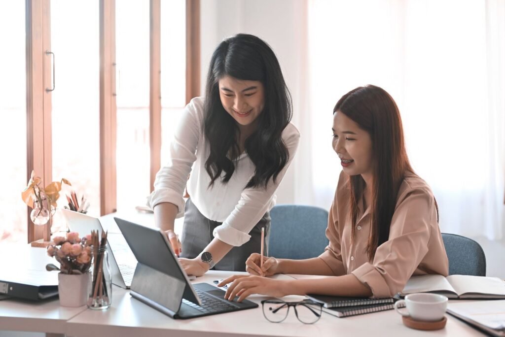 Two smiling women collaborate, analyzing website user behavior on a laptop for CRO and UX optimization.