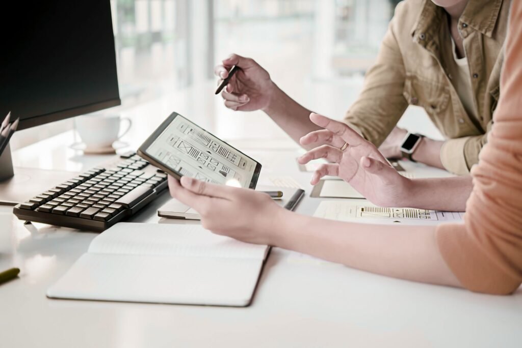Two designers review tablet wireframes, collaborating on innovative UI/UX solutions for digital growth.