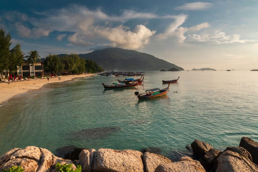 Phuket's picturesque beach with traditional longtail boats on clear turquoise water, a sandy shore, and lush trees.
