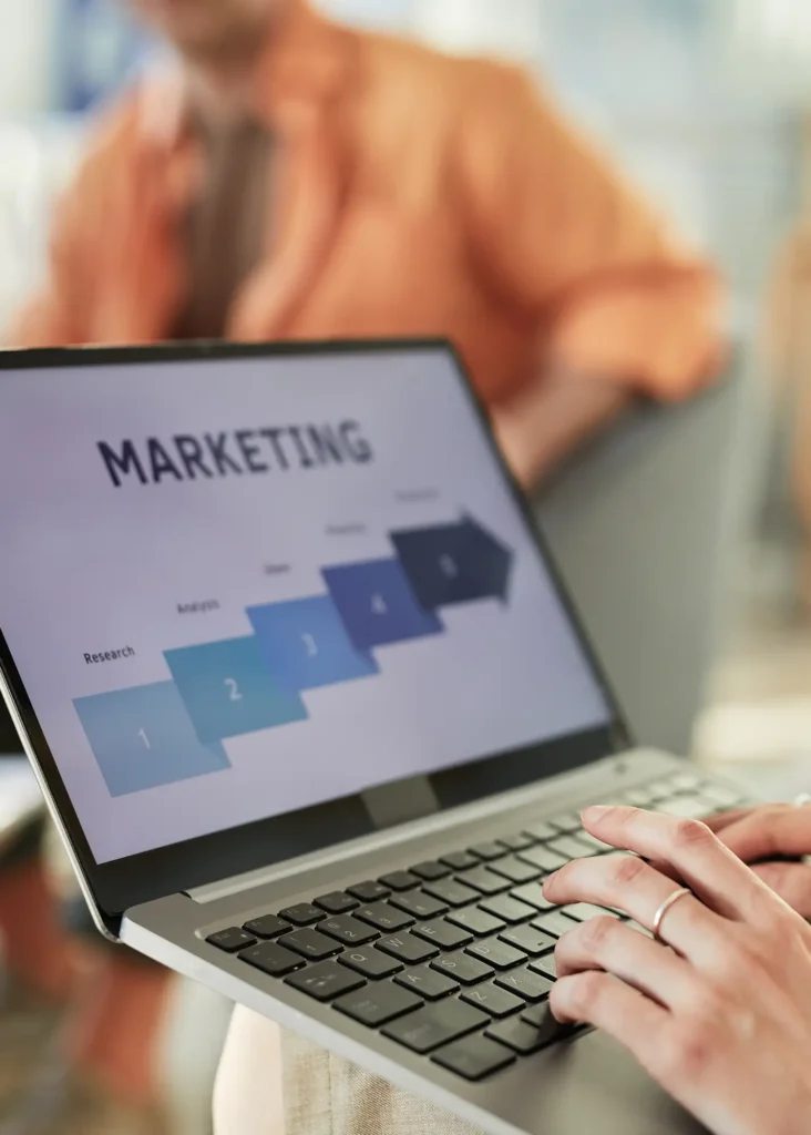 Hands typing on a laptop displaying a "MARKETING" process diagram, reflecting expert strategy for paid media services.