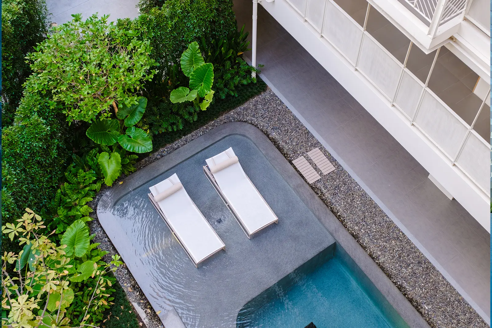 Aerial view of a luxurious Citadel Real Estate property in Bangkok: modern pool with lounge chairs, lush tropical garden.