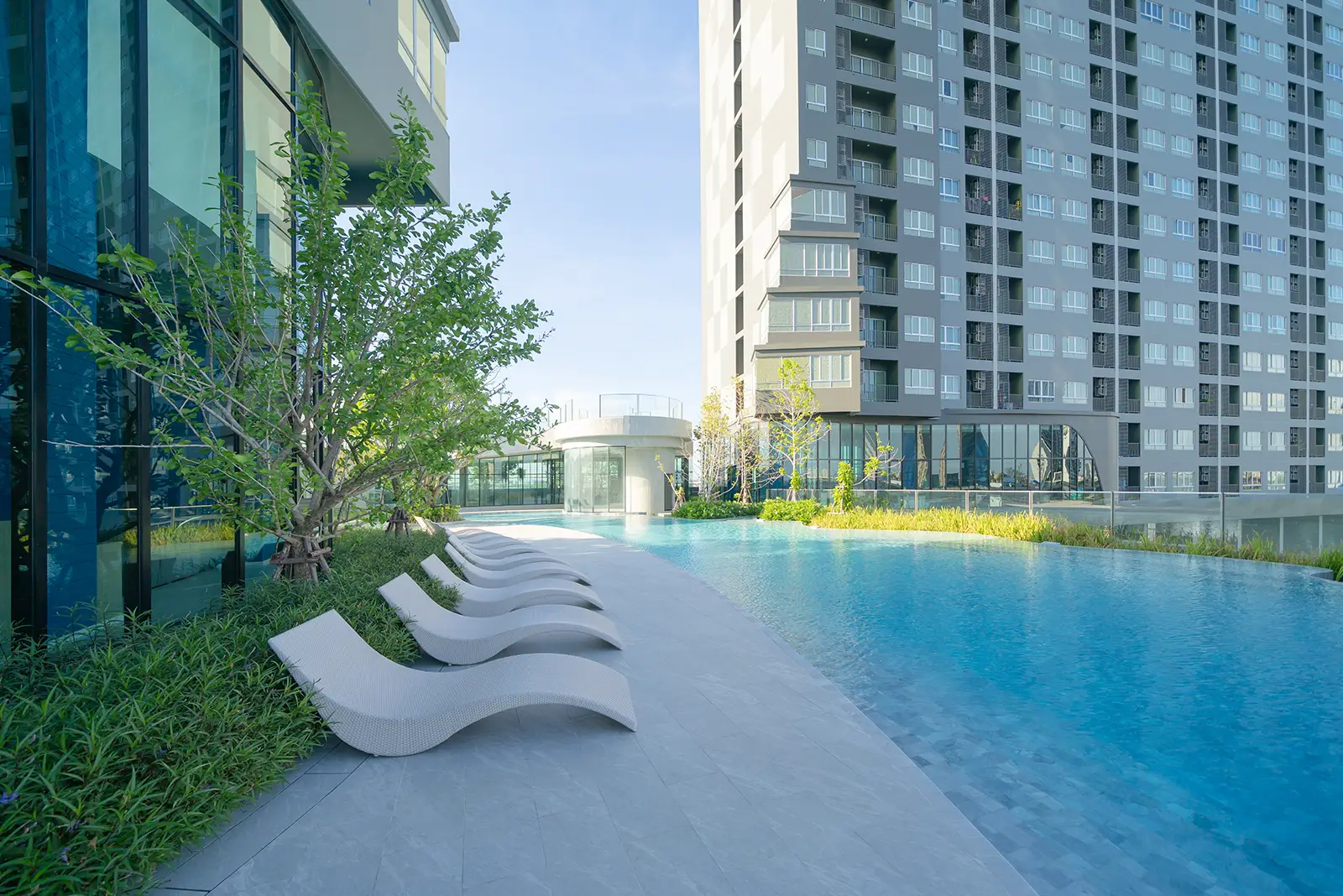 Modern high-rise real estate property in Bangkok with a large swimming pool and lounge chairs, showcasing Citadel's offerings.