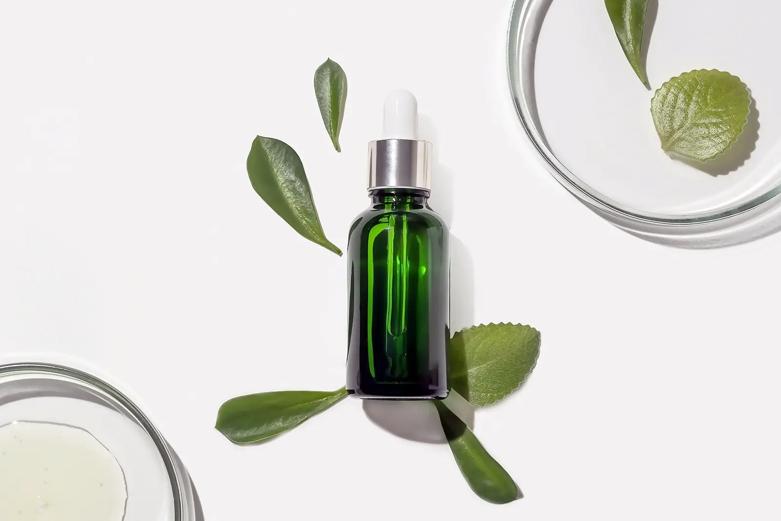 Green organic serum bottle, fresh leaves, and lab dishes, illustrating Goodganic's natural products for our marketing strategy.