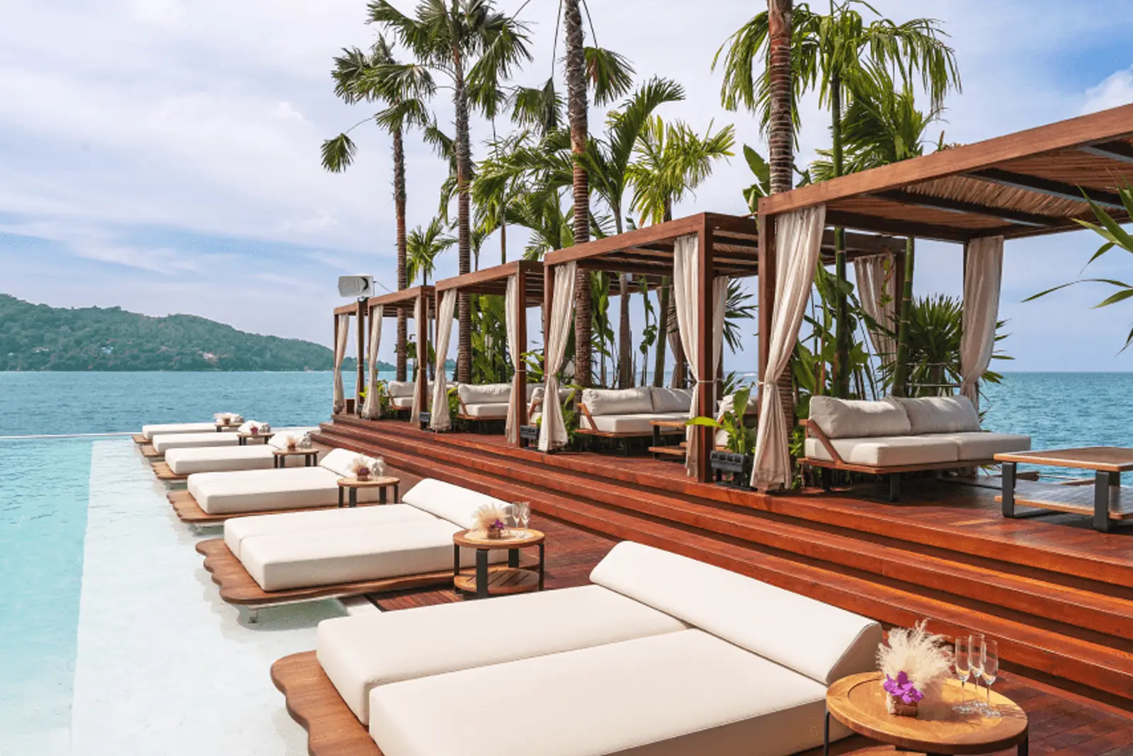 Yona Beach Club's floating deck: infinity pool, ocean, palm trees, and elegant cabanas, highlighting its allure.